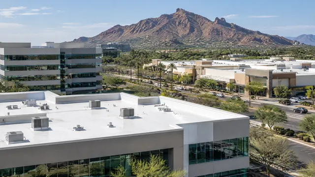 Rooftops of modern office buildings and a retail center along the Camelback Corridor in Phoenix with Camelback Mountain behind, flat white roofs and parapets