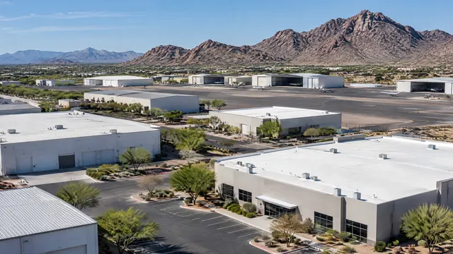 Industrial park and small airport hangars in the Deer Valley area of north Phoenix, flat and low-slope metal and white membrane roofs, rocky desert hills behind