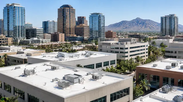 Elevated view over flat rooftops of mid-rise commercial buildings in downtown Phoenix, white roofs with HVAC units, high-rise towers behind and South Mountain in the distance