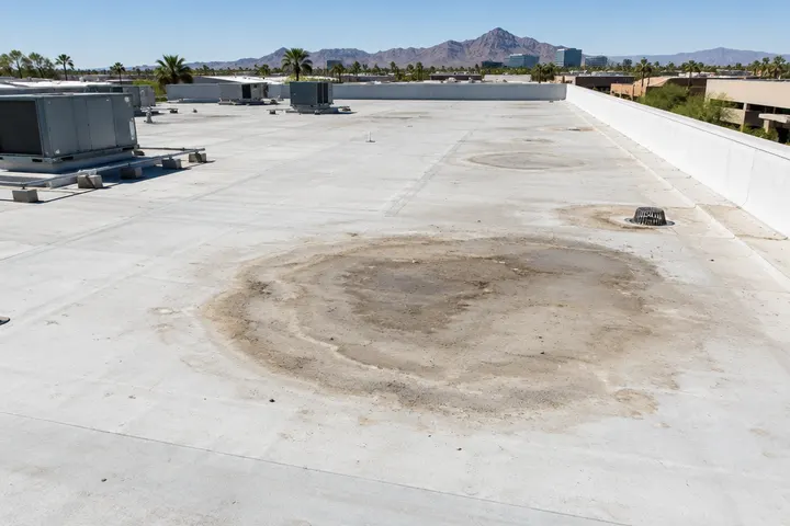 Wide flat commercial roof with dried ponding rings and dirt marks in a low spot away from the drain