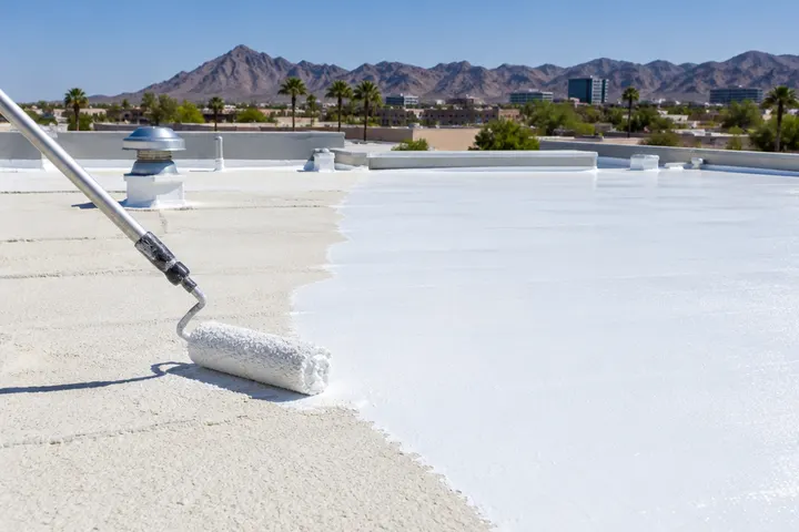 Roller applying bright white silicone roof coating over a foam roof, half coated, half bare